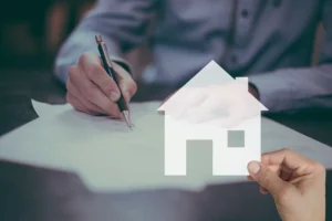 Personne écrivant des notes financières à côté d’une maquette de maison, illustrant la gestion du patrimoine immobilier et l’optimisation de l’impôt sur la fortune immobilière (IFI).